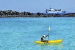 Man kayaking in crystal blue oceans with Los Angeles Pinta ship in background